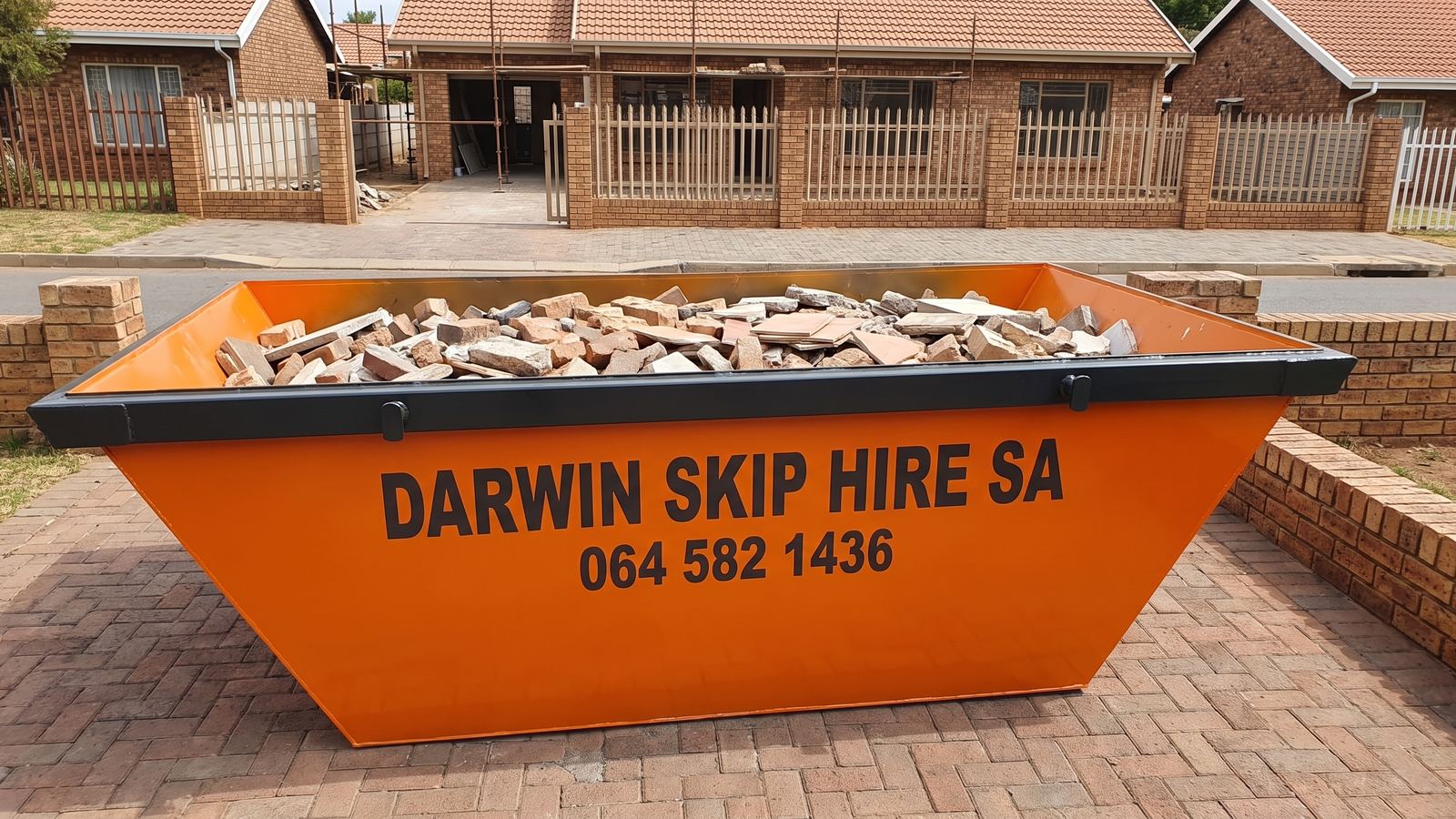 Orange Darwin Skip Hire SA skip loaded with broken bricks and tiles outside a house under renovation.