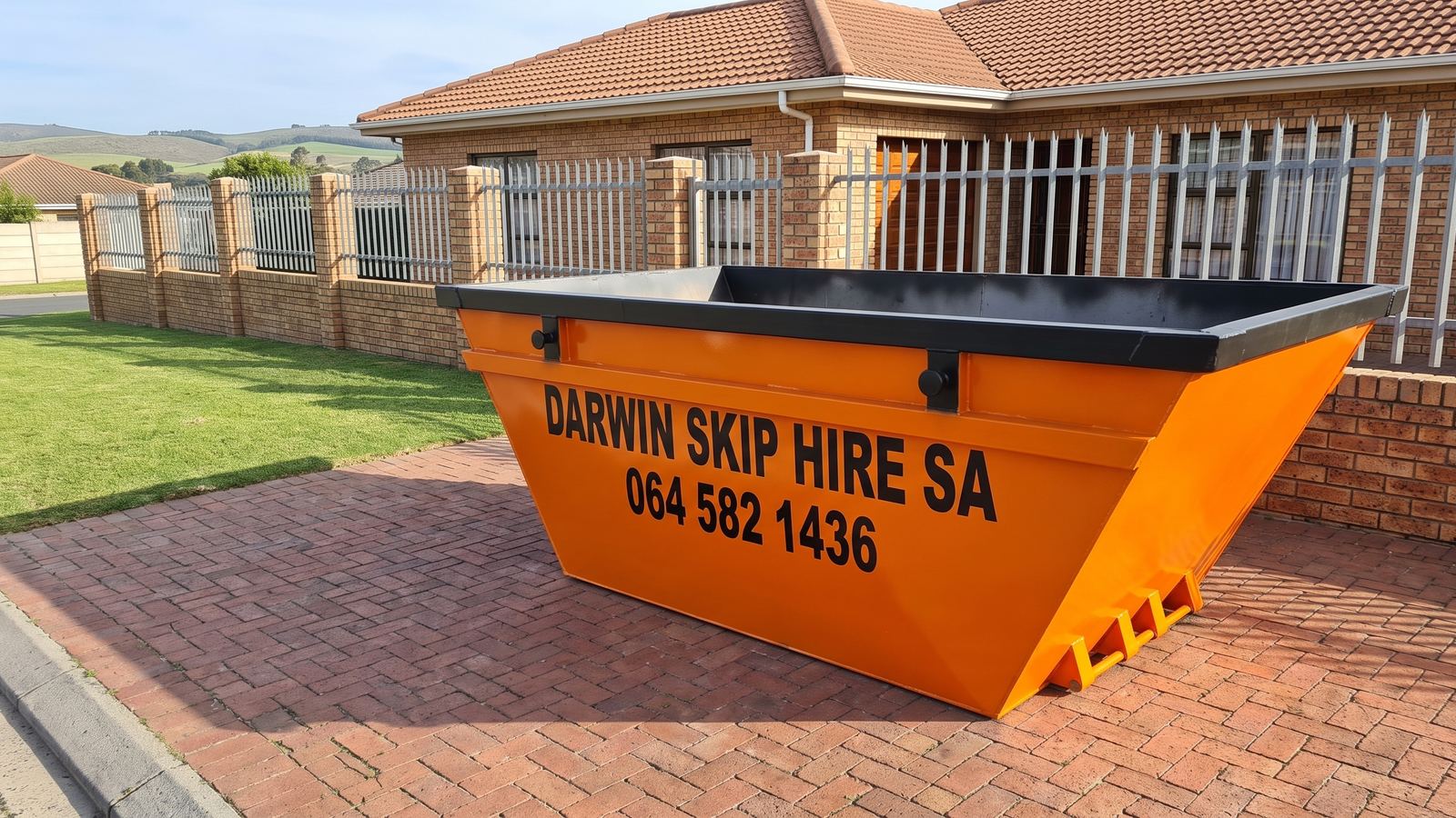 Orange Darwin Skip Hire SA mini skip standing empty on a brick-paved driveway.