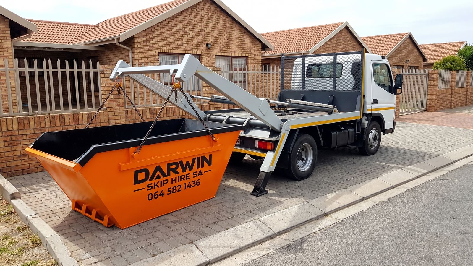 Skip-loader truck lowering an orange Darwin Skip Hire SA skip on chains in front of a face-brick home.